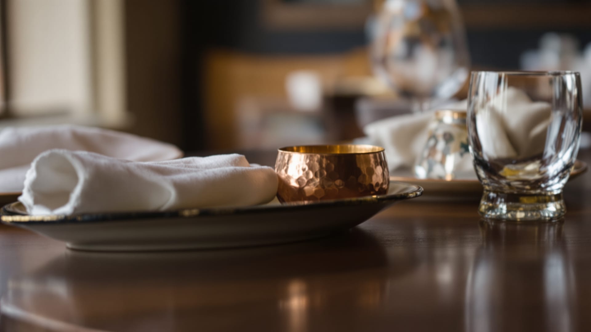 Detail of a set table in a closed Indian restaurant, water glass and folded napkin beside a small copper bowl